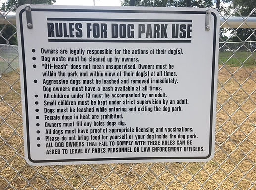 Close-up of a posted sign listing detailed rules for dog park use, mounted on a chain-link fence.