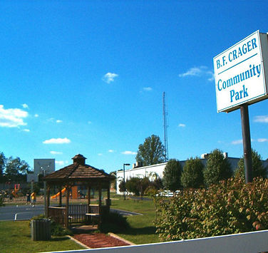 Entrance area of B.F. Crager Community Park featuring a wooden gazebo, basketball court, and community sign under a clear blue sky.