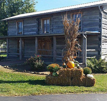 Restored log cabin decorated for fall with hay bales, pumpkins, and corn stalks, located in B.F. Crager Community Park.
