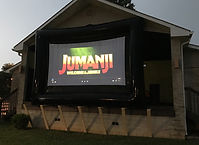 Inflatable outdoor movie screen displaying “Jumanji: Welcome to the Jungle” set up in front of the stage at dusk in B.F. Crager Community Park.