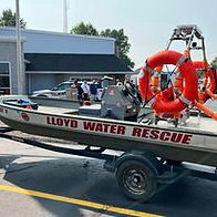 An emergency response boat labeled “Lloyd Water Rescue” is mounted on a trailer, equipped with multiple orange life preservers and displayed outside a public safety building.