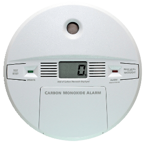 Close-up of a round carbon monoxide alarm with a digital display reading “0,” green and red indicator lights labeled “Operate” and “Alarm,” and a button labeled “Test/Reset.” The alarm features text stating “Carbon Monoxide Alarm” and includes a small speaker grill and backlight indicator.