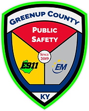 Shield-shaped emblem for Greenup County Public Safety in Kentucky. The badge is divided into sections: the top red area says “Public Safety” with “Since 2019” in a white circle, the left yellow section has a green “E911” logo, the right gray section features a blue “EM” with stars, and the bottom blue banner reads “KY.” The border is outlined in green and blue.